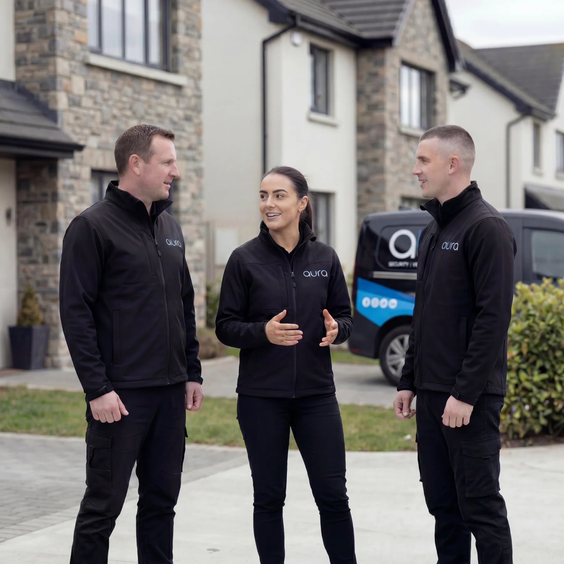 Three Aura Smart team members in branded jackets talking outside a home, with the Aura van behind them
