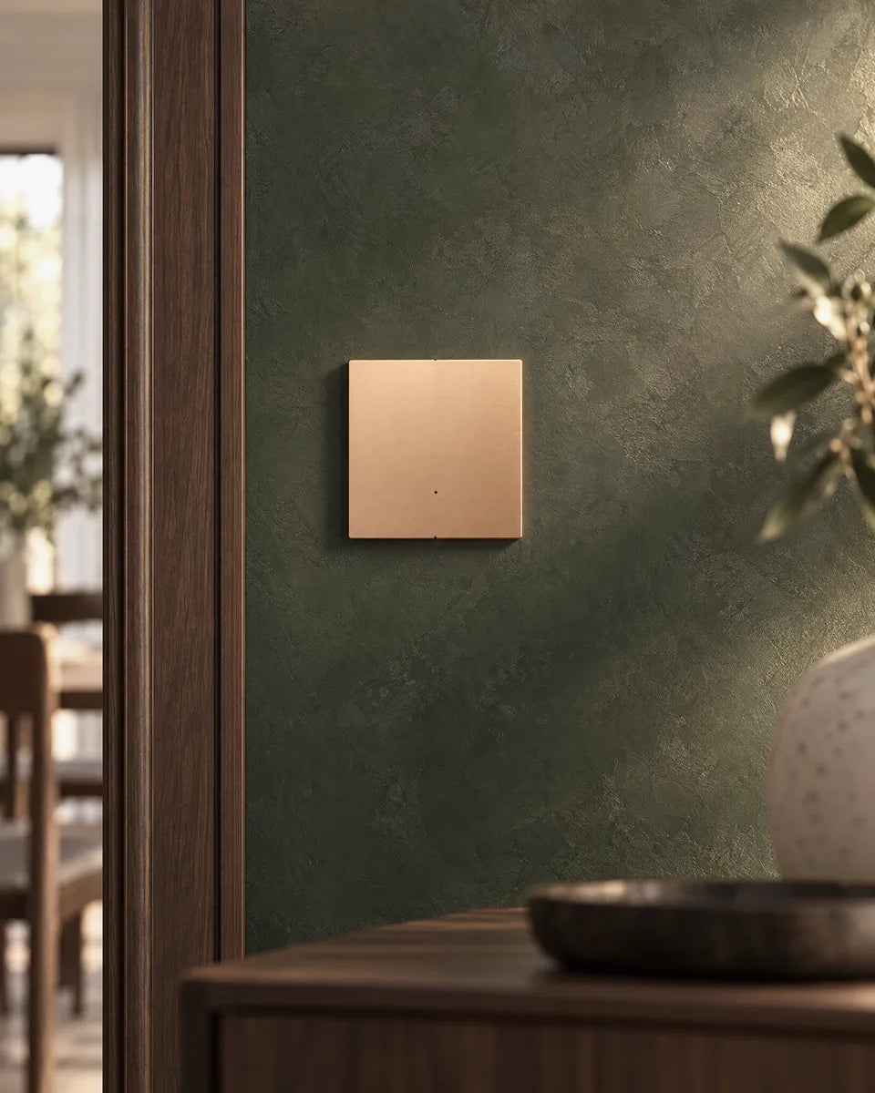 A gold aluminium 1-gang smart light switch on a deep green plaster wall beside a walnut door frame